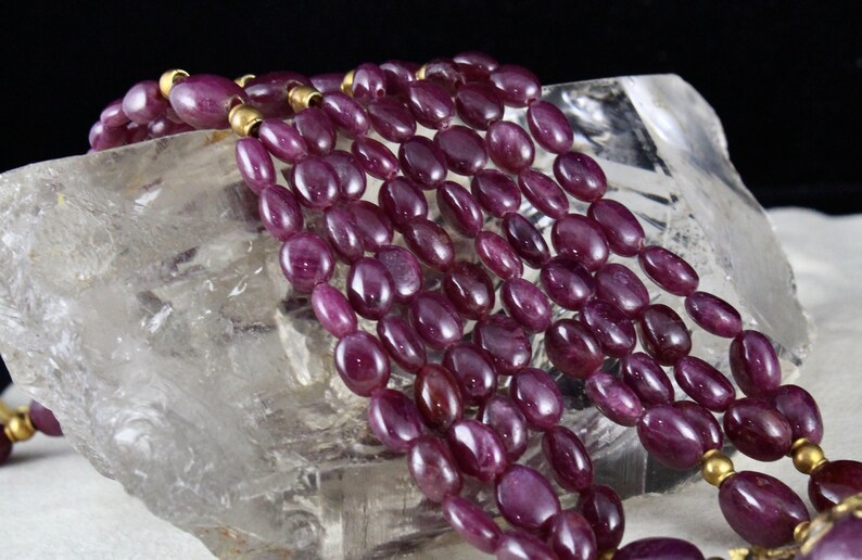 Pu&ograve; includere: Una collana multifilo realizzata con perline di rubino ovali di colore viola scuro con distanziatori dorati.