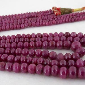 May include: A multi-strand necklace composed of deep red, polished beads. The beads vary in size, with larger, rounded beads at the bottom. The necklace has a tassel and cord closure. Jewelry.
