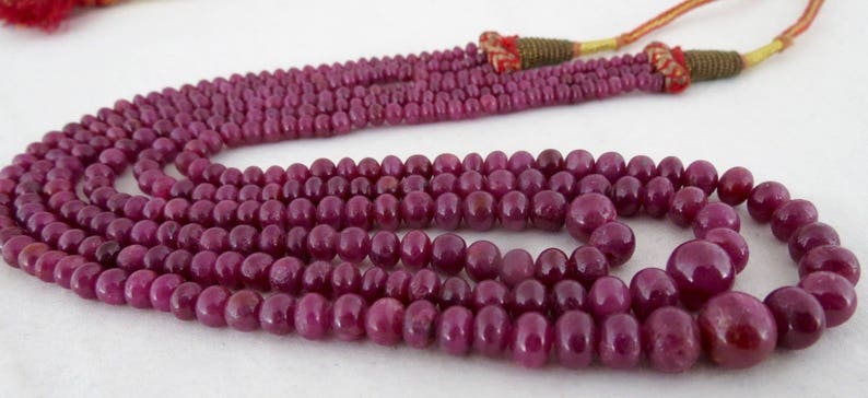 May include: A multi-strand necklace composed of deep red, polished beads. The beads vary in size, with larger, rounded beads at the bottom. The necklace has a tassel and cord closure. Jewelry.