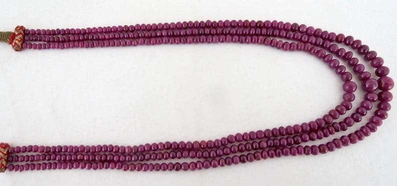 May include: A multi-strand necklace composed of small, round, deep red beads. The necklace has a woven closure at each end. The beads are strung together to create a layered effect, suitable for jewelry.