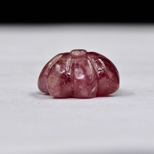 May include: A carved pink gemstone with a rounded, scalloped shape.