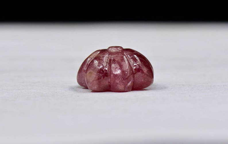 May include: A carved pink gemstone with a rounded, scalloped shape.