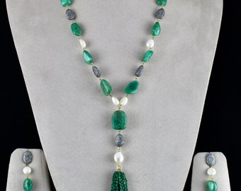Puede incluir: Un collar de piedras preciosas verdes con un colgante de borla y pendientes a juego. El collar presenta piedras verdes, perlas blancas y detalles de diamantes negros.