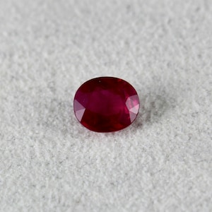 May include: A deep red oval-shaped gemstone with a smooth, polished surface.