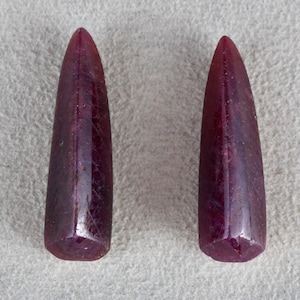 May include: Two dark red ruby gemstones, each shaped like a long, pointed teardrop.