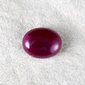 Puede incluir: Una piedra preciosa ovalada de color rojo intenso con una superficie lisa y pulida.