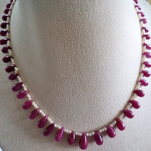 Op de afbeelding: Een ketting gemaakt van afwisselende witte parels en druppelvormige robijnrode stenen.