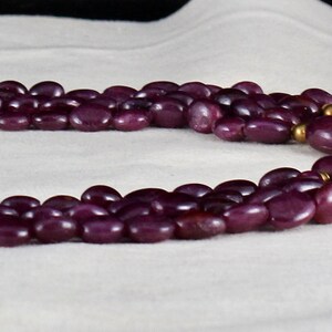 Pu&ograve; includere: Una collana multifilo realizzata con perline viola scuro con accenti dorati. La collana presenta due grandi ciondoli con disegni intricati e pietre preziose verdi.