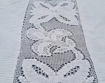 Könnte beinhalten: Handgefertigter, weißer Häkeltischläufer mit einem komplizierten Blumen- und geometrischen Design. Der Läufer ist auf einer weißen, strukturierten Oberfläche zentriert und zeigt das detaillierte Lochmuster. Die Länge und die filigrane Handwerkskunst des Läufers sind hervorstechend.