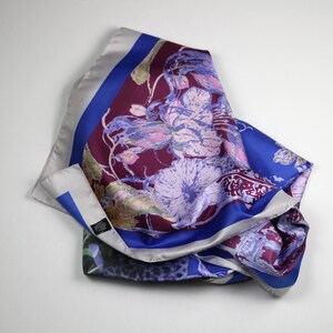 May include: A silk scarf with a floral print in shades of pink, purple, and blue. The scarf has a burgundy background with a blue border and a silver border.