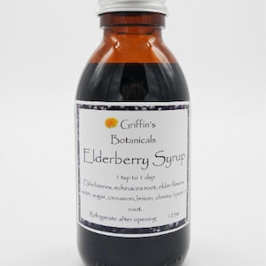 May include: A brown glass bottle with a silver lid, labelled "Griffin's Botanicals Elderberry Syrup". The label also includes instructions for use and a list of ingredients, including elderberries, echinacea root, elder flowers, water, sugar, cinnamon, lemon, cloves, and honey root. The bottle is sitting on a white surface.