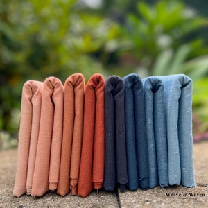 May include: Eight folded fabric swatches in various shades of pink, orange, red, gray, blue, and light blue. The fabric has a subtle crosshatch pattern. The text "Weave & Woven" is visible at the bottom of the image.