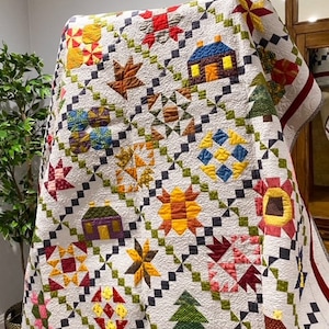 May include: A white quilt with a patchwork design featuring various shapes and colors, including red, green, yellow, and brown. The quilt is made up of squares and triangles, and it has a border of red and white.
