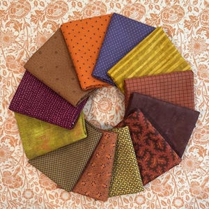 May include: A collection of colorful fabric swatches arranged in a circular pattern. The fabrics feature various patterns, including polka dots, stripes, and floral designs, in shades of orange, purple, green, and brown. The background is a floral patterned fabric.