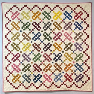 May include: A white quilt with a red border and a repeating pattern of colorful squares arranged in a geometric design.