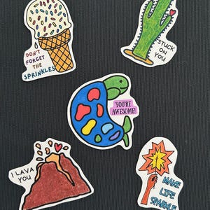 May include: Five colorful stickers with different designs and messages. The stickers feature a cactus with the text "Stuck on you", a turtle with the text "You're awesome!", a volcano with the text "I lava you", an ice cream cone with the text "Don't forget the sprinkles", and a hand holding a sparkler with the text "Make life sparkle".