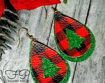 May include: A pair of dangle earrings with a red and black buffalo plaid pattern and a green glitter Christmas tree design. The earrings are made of leather and have gold-colored hooks.