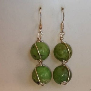 May include: A pair of silver dangle earrings with two green gemstone beads on each earring. The beads are wrapped in silver wire.