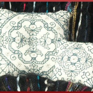 Puede incluir: Dos almohadas blancas bordadas con un diseño geométrico en hilo azul oscuro. Las almohadas están sobre una tela con estampado negro y azul.