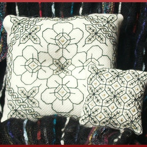 Könnte beinhalten: Zwei weiße Kissenbezüge mit schwarzen und goldenen Stickereien. Das größere Kissen zeigt ein sich wiederholendes Muster aus stilisierten Blumen. Das kleinere Kissen zeigt ein sich wiederholendes Muster aus stilisierten Blättern.