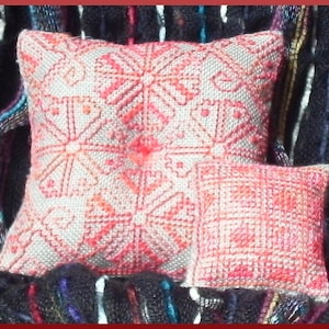Puede incluir: Dos almohadas pequeñas, cuadradas y decorativas con fondo blanco y bordado floral rosa. Las almohadas están hechas de una tela suave y texturizada.
