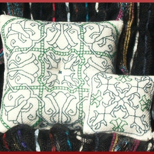 Puede incluir: Dos almohadas blancas con diseños bordados en verde y negro. Las almohadas están sobre una tela de rayas blancas y negras.
