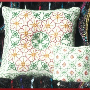Puede incluir: Dos almohadas bordadas, una con un patrón floral en tonos de blanco, rojo y amarillo, y la otra con un patrón geométrico en verde y blanco.