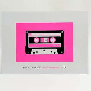 Puede incluir: Un póster de temática retro con un diseño de cinta de cassette en blanco y negro sobre un fondo rosa brillante. El póster incluye el texto "BACK TO THE EIGHTIES" y "SK-90". La obra de arte está montada sobre un fondo blanco.