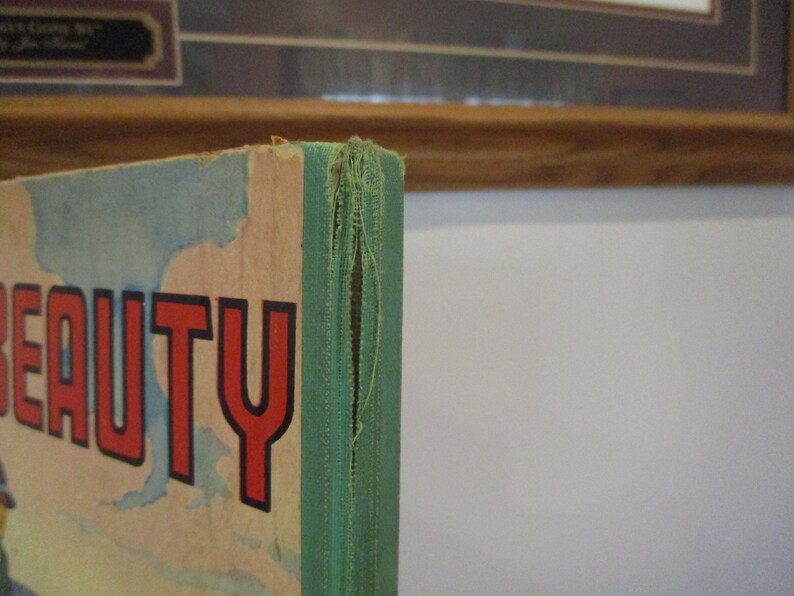 May include: Close-up of a vintage book cover with the word "BEAUTY" in large red letters. The cover has a distressed, aged appearance with a green spine and visible wear and tear.