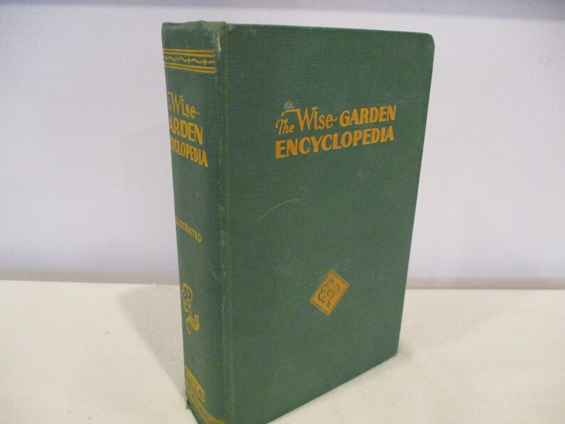 Puede incluir: Un libro de tapa dura verde titulado "The Wise-Garden Encyclopedia". El libro tiene letras doradas y una ilustraci&oacute;n dorada de una flor en la portada.