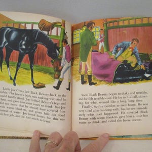 May include: An open book with illustrations from a children's story. One page shows a black horse in a stable, and the other depicts a man tending to the horse. Text accompanies the illustrations.