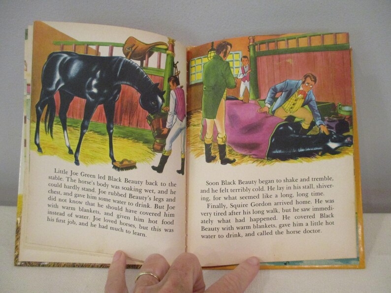 May include: An open book with illustrations from a children's story. One page shows a black horse in a stable, and the other depicts a man tending to the horse. Text accompanies the illustrations.