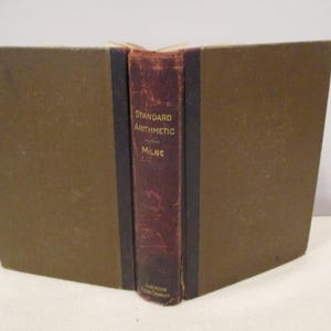 May include: An open book with a brown cover and a maroon spine. The spine reads "Standard Arithmetic" by Milne, with "American Book Company" at the bottom. The book's pages are visible.