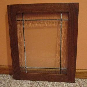 Puede incluir: Una ventana con marco de madera, un panel de vidrio transparente y una cuadrícula de barras de metal negro.
