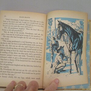 May include: Open book with text and an illustration of a black horse with two men. The illustration is in blue and black. The text on the left page is titled "BLACK BEAUTY".