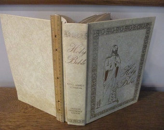 May include: A white leather-bound Holy Bible with gold lettering and a gold-framed illustration of Jesus on the front cover. The text on the spine reads "Holy Bible King James Version Division Reference Edition".