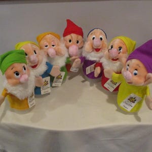 Puede incluir: Una colección de siete muñecos de peluche que representan a los Siete Enanitos de Blancanieves. Cada enanito tiene un color de sombrero, atuendo y expresión facial únicos. Los muñecos tienen etiquetas.