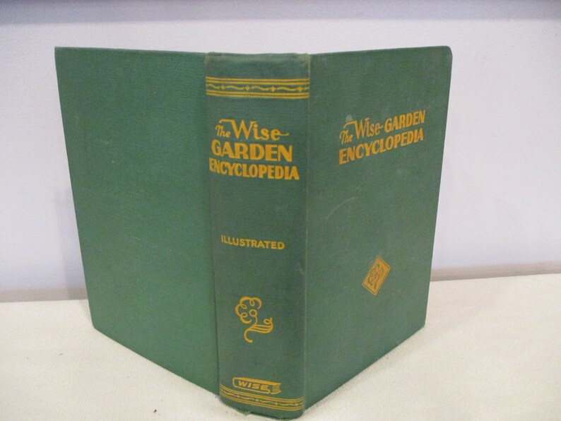 Puede incluir: Un libro de tapa dura verde titulado "The Wise Garden Encyclopedia" con letras doradas. El libro est&aacute; ilustrado y tiene un dise&ntilde;o de &aacute;rbol dorado en el lomo.