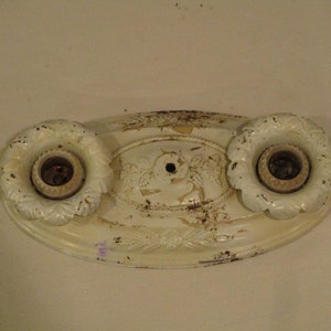 May include: White oval ceiling light fixture with two sockets and ornate details. The fixture has a worn, aged appearance.
