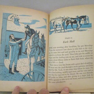 May include: Open book with illustrations in blue and white. One illustration shows a man on horseback, another shows horses in a stable. Text on the right page reads "Chapter 23 Earls Hall".