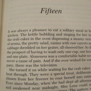 Puede incluir: Un primer plano de una p&aacute;gina de libro con el t&iacute;tulo "Fifteen" y texto sobre una mujer que disfruta de una comida solitaria en su cocina. El texto describe la tetera hirviendo, las tartas de cangrejo en el horno y una ensalada con pasas y col rallada.