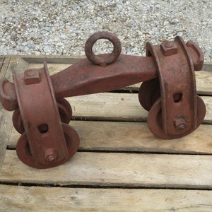 Könnte beinhalten: Ein rostiges Metall-Rollensystem mit zwei Rädern und einem Ring oben. Das Rollensystem steht auf einer Holzkiste.