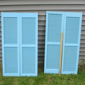 May include: Two sets of blue wooden shutters with louvers. Each set has two panels.
