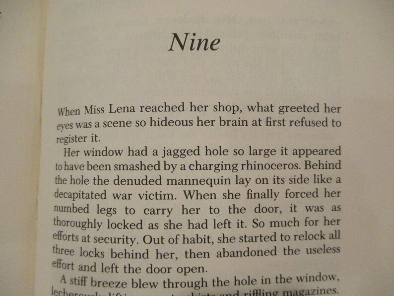 Puede incluir: Una p&aacute;gina de un libro con el t&iacute;tulo "Nueve" y un p&aacute;rrafo de texto sobre una due&ntilde;a de una tienda que encuentra su tienda en desorden. El texto describe un gran agujero en la ventana y un maniqu&iacute; acostado de lado.