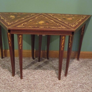 May include: A triangular wooden side table featuring dark brown wood grain, tapered legs, and intricate gold-toned floral inlay patterns on the tabletop surface. The table has a smooth finish and decorative detailing along the legs and edges.