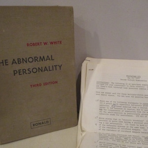 Op de afbeelding: Een vintage boek getiteld "The Abnormal Personality" van Robert W. White, derde editie, met een bruine kaft en rode letters. Daarnaast liggen examenpapieren van een psychologiecursus.