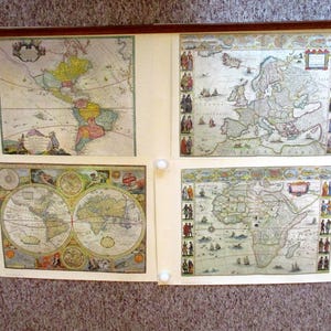 May include: A collection of four antique world maps, each with intricate details and vibrant colors. The maps are displayed on a cream-colored background, held together by white push pins and a dark brown wooden rod at the top. The maps depict continents and oceans.