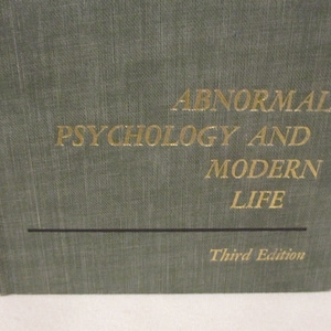 Op de afbeelding: Een groen boek met gouden letters op de omslag. De titel is "Abnormale Psychologie en het moderne leven" en de ondertitel is "Derde editie".