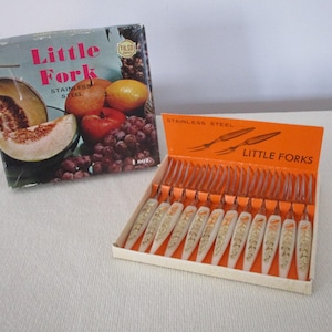 May include: Vintage set of "Little Forks" in a box. The box features a fruit illustration and the text "Little Fork Stainless Steel". The forks have white handles with gold floral designs. The box is orange and white.