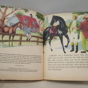 May include: Vintage children's book illustration featuring two horses, one brown and one black, with a boy and two men. The book is open, displaying colorful images and text about the story of Black Beauty.